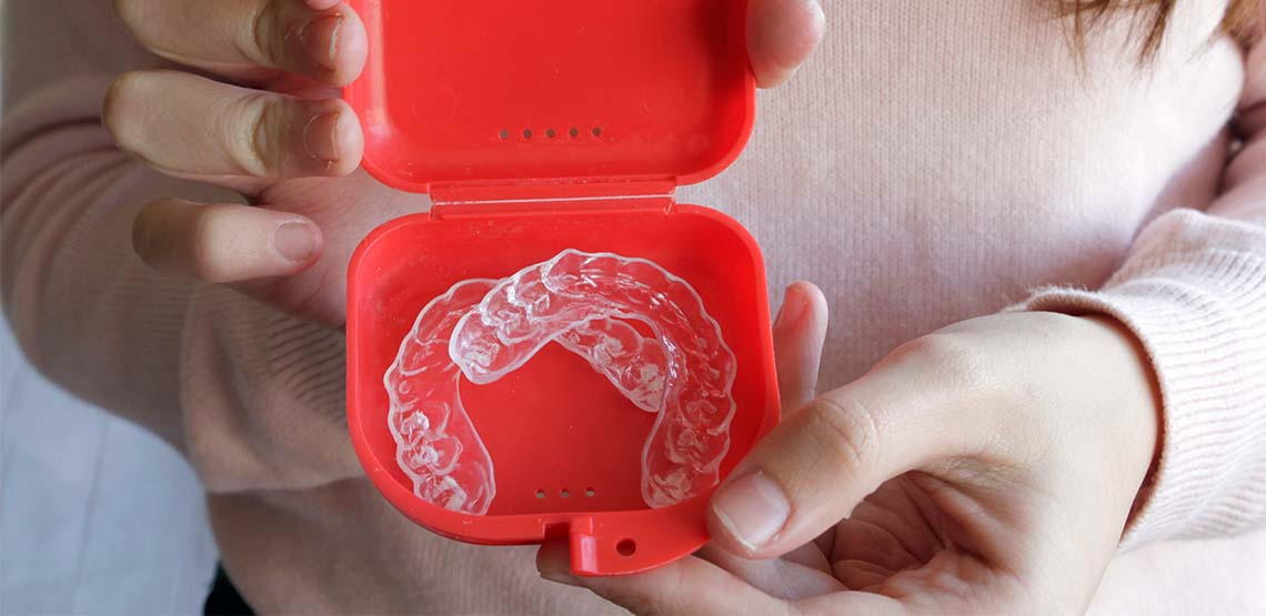 A person holding a red case with two aligners in it.